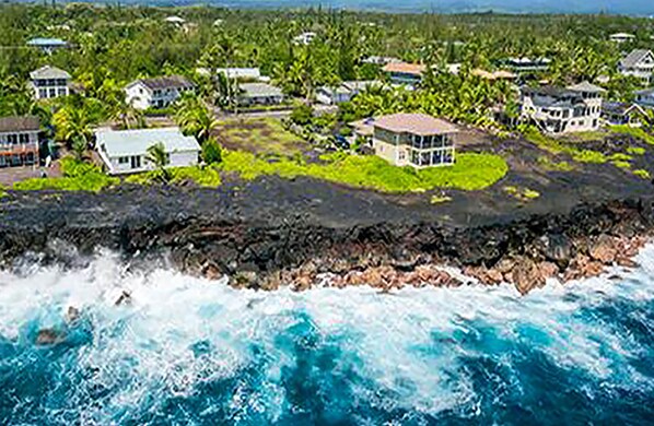 A coastal residential area with houses surrounded by lush greenery and a rocky shoreline.