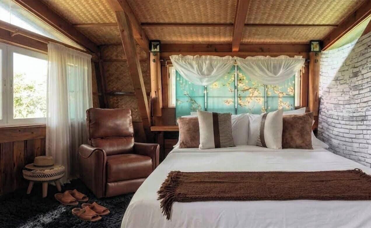 A bedroom with a bed, a leather chair, a small round table, and a window with curtains.