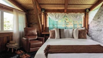 A bedroom with a bed, a leather chair, a small round table, and a window with curtains.