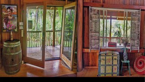 Una baita di legno con un portico, una porta che si apre verso l'esterno e una finestra con vista sul verde.