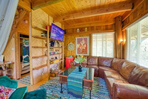 A cozy living room with a brown leather couch, a glass coffee table, and a TV on a wooden shelf.