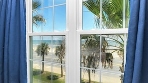Ein Fenster mit Blick auf einen Strand, Palmen und einen klaren, blauen Himmel.