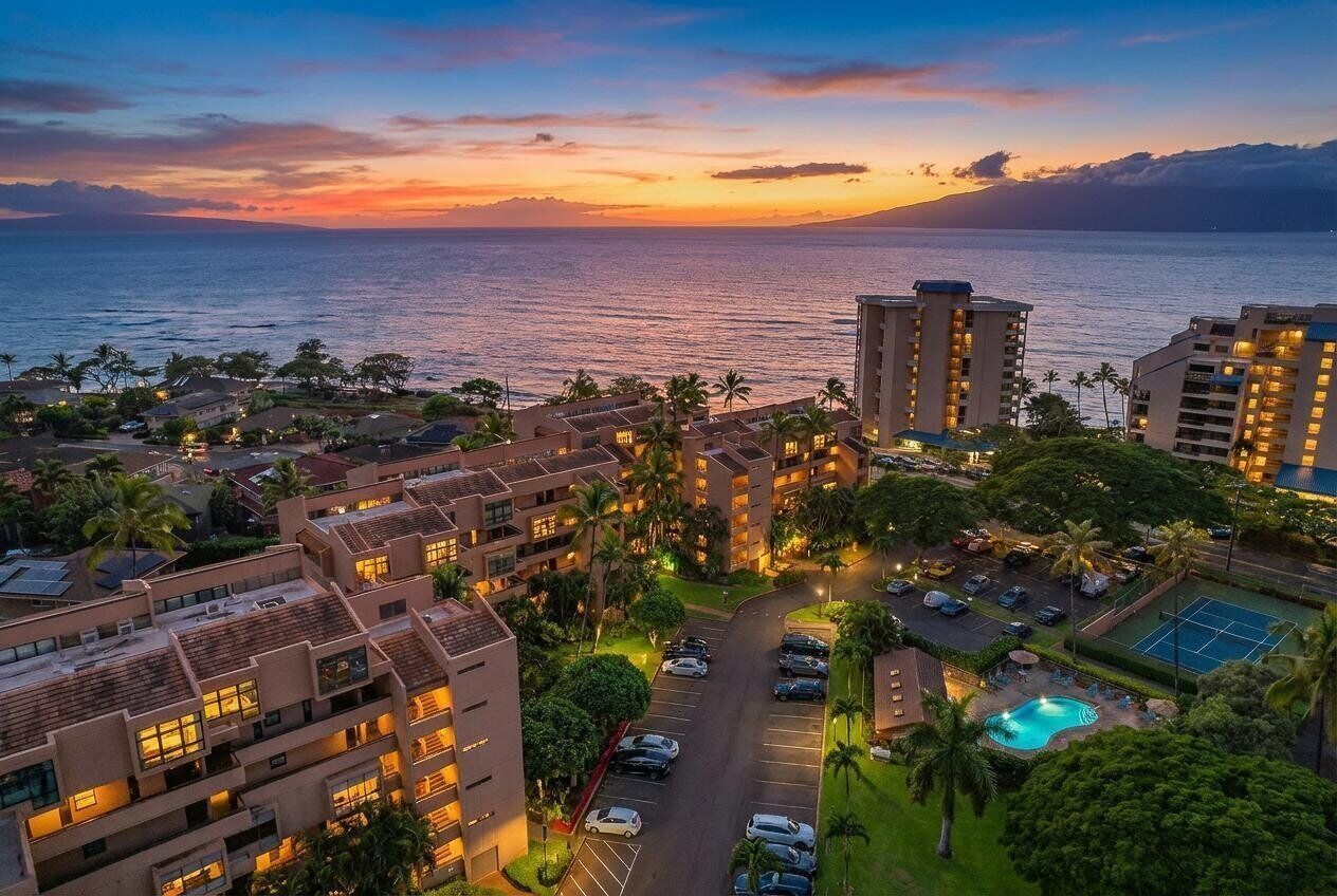 A hotel with multiple buildings, a swimming pool, and a view of the ocean at sunset.