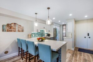 A modern kitchen with a marble island, two pendant lights, and a stainless steel refrigerator.