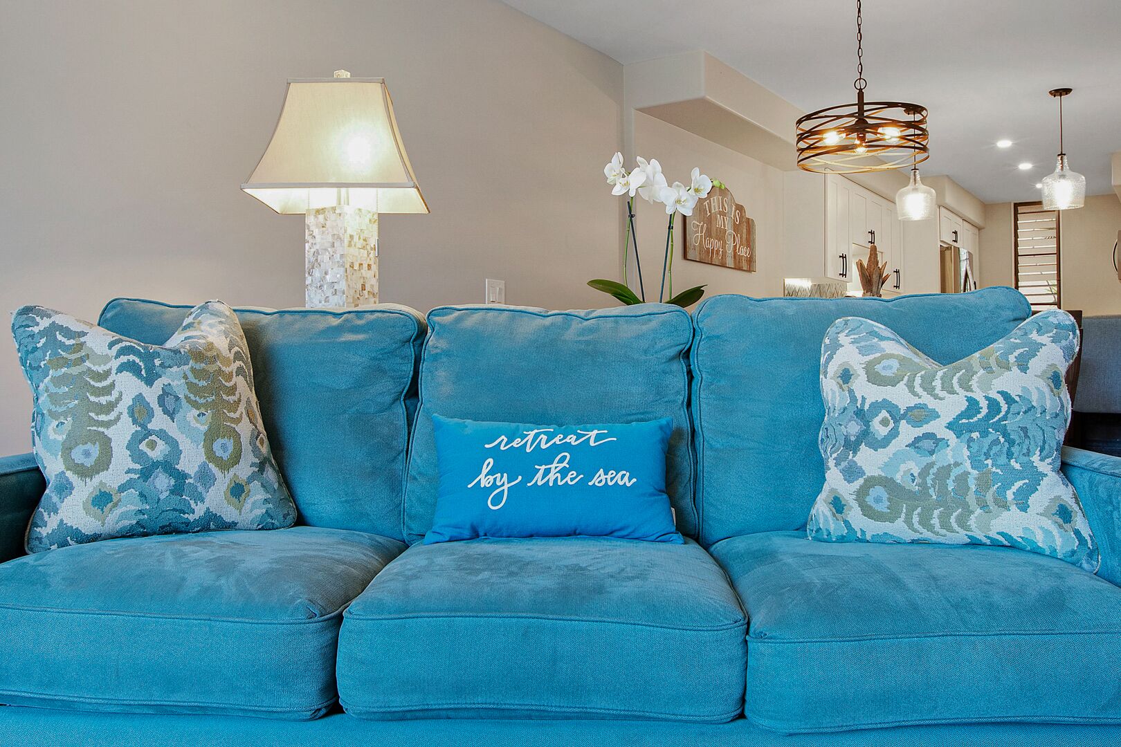 Ein blaugrünes Sofa mit gemusterten Kissen und einem Kissen mit dem Aufdruck 'retreat by the sea'.