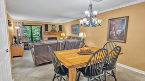 A dining area with a wooden table and black chairs, a chandelier, and a fireplace in the background. - two bedroom condo sleeps 4 persons (Gatlinburg)