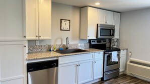 Una cocina con gabinetes blancos, encimera de granito, lavavajillas de acero inoxidable, microondas, horno y cafetera.
