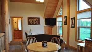 A cozy dining area with a round wooden table, four chairs, a wooden bench, and a television mounted on the wall.
