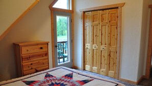 A bedroom with a large bed, a wooden dresser, a door leading to a balcony, and a wooden closet.