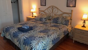 Ein Schlafzimmer mit einem Bett, zwei Nachttischen mit Lampen, einer Tür und zwei an der Wand befestigten Kunstwerken.