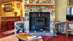 Una sala de estar con chimenea de piedra, un banco de madera y un televisor.
