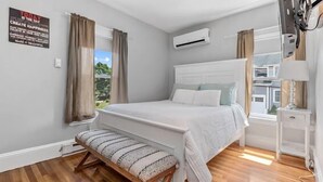 Een slaapkamer met een bed, een bankje, een airconditioner en een televisie.