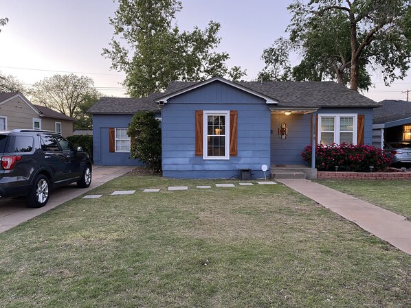 A residential house with a blue exterior, a front yard with stepping stones, and a parked SUV.