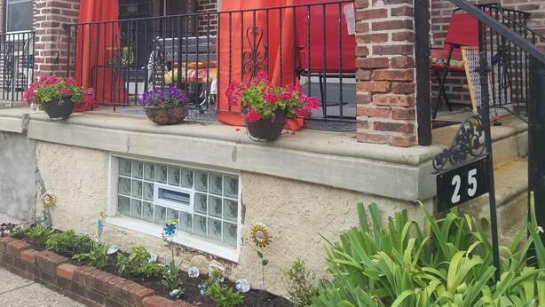 En bygning med murstensfacade, en overdækket veranda med røde gardiner og krukker med planter.