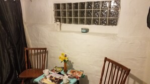 Et lille værelse med to træstole, et bord med rejsemagasiner, en vase med gule blomster og et vindue med sandblæst glas.