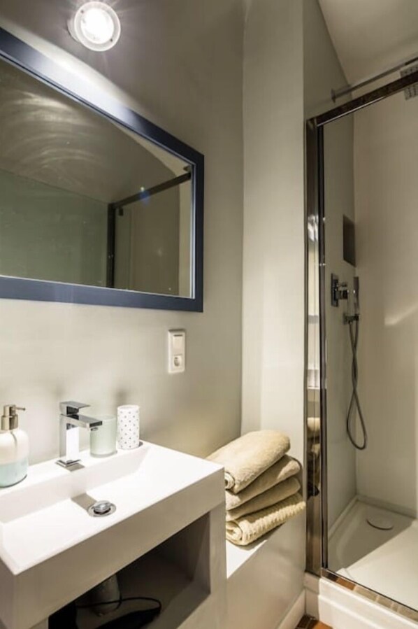 Un baño moderno con ducha de vidrio, un lavamanos blanco con espejo y un perchero para toallas.