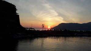 A sunset over a body of water with a silhouette of a building on the left and mountains in the background. - Residential flat in Vernazza, natural park of 5 Terre (Vernazza)