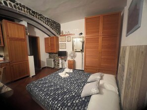 Une chambre à coucher avec un lit, une armoire en bois, une télévision et un ventilateur.