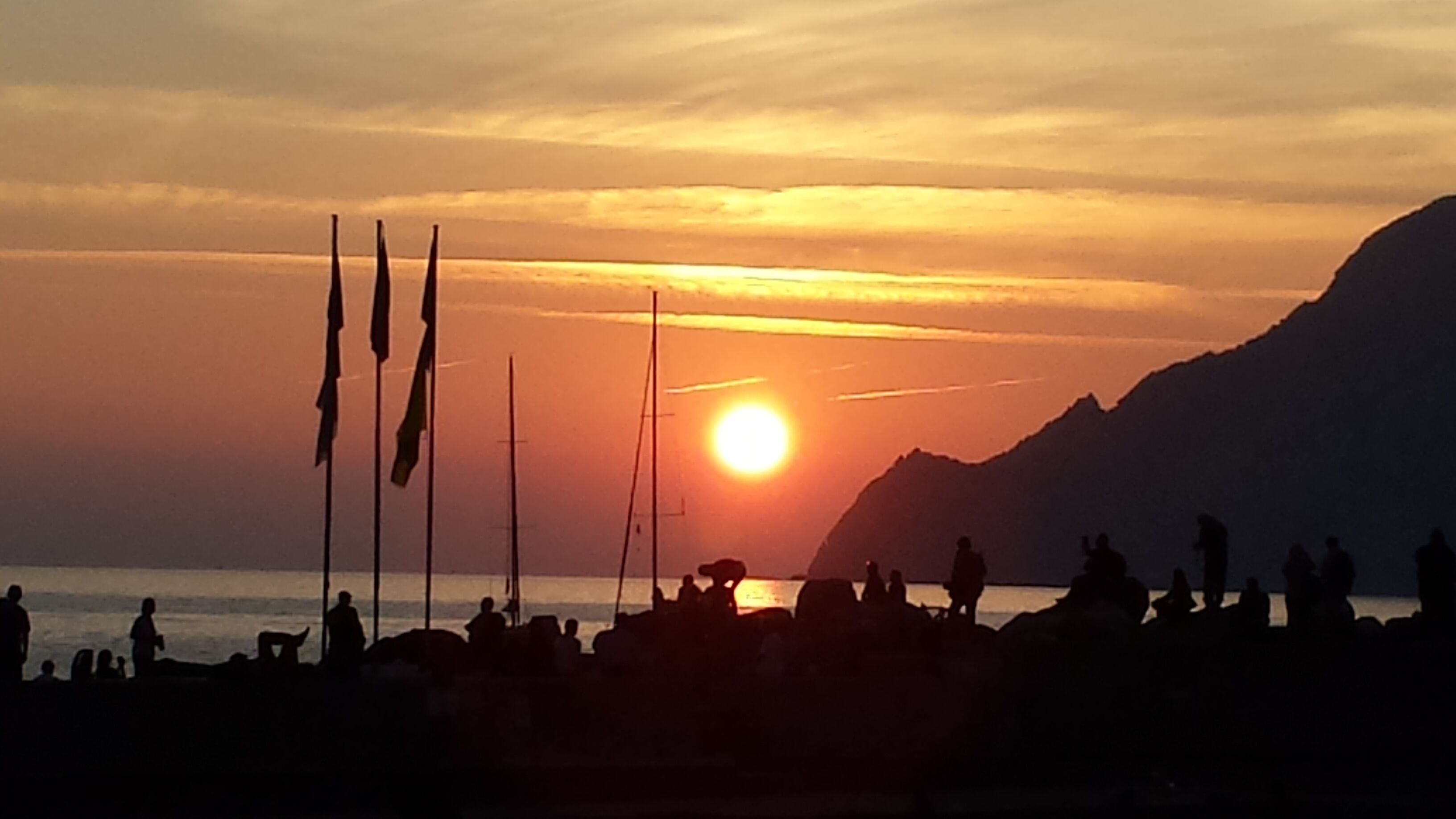 A sunset over a beach with silhouettes of people and a mountain in the background.