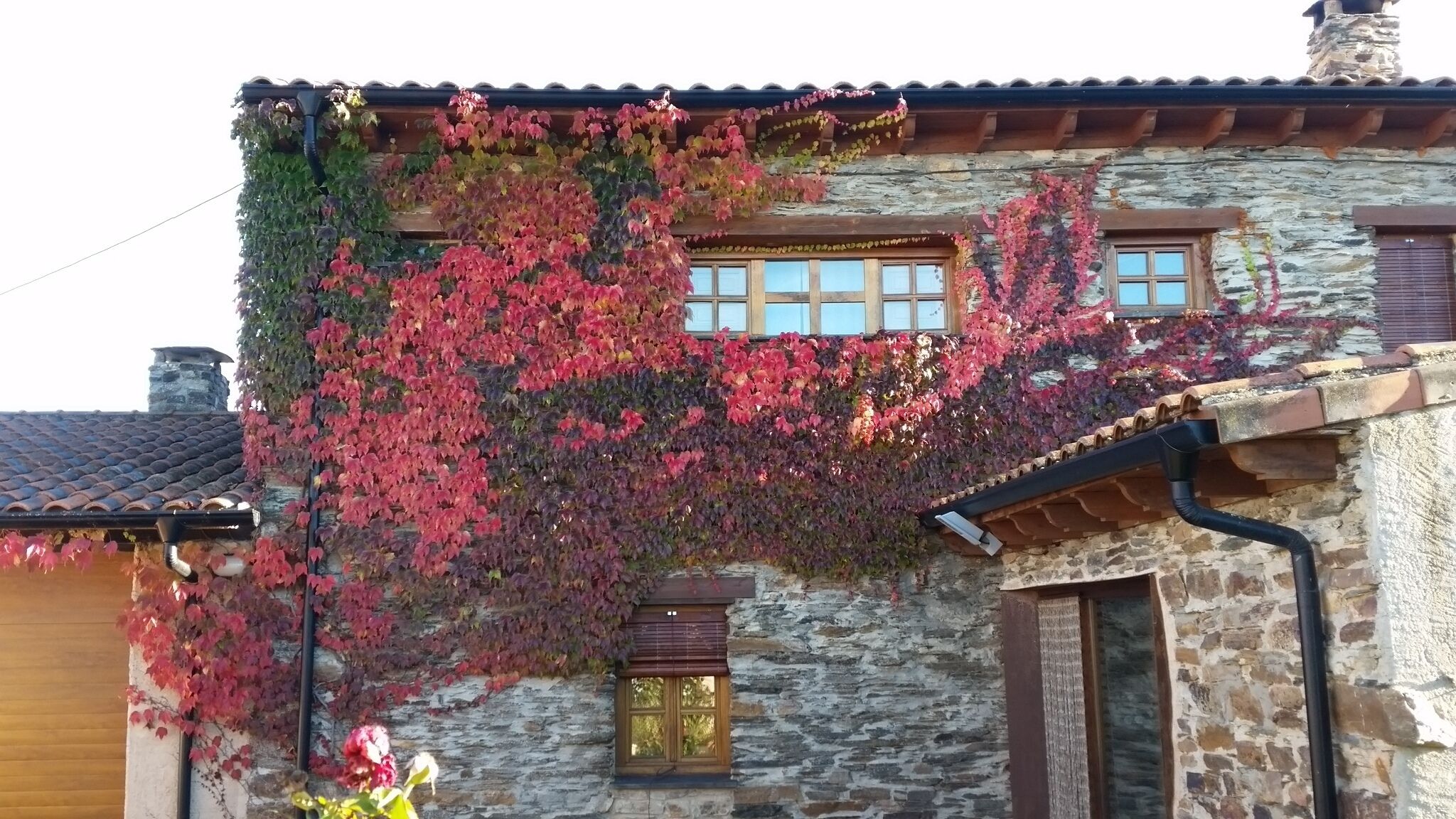 Un edificio de piedra con techo de tejas, marcos de madera para las ventanas y una pequeña ventana con persiana.