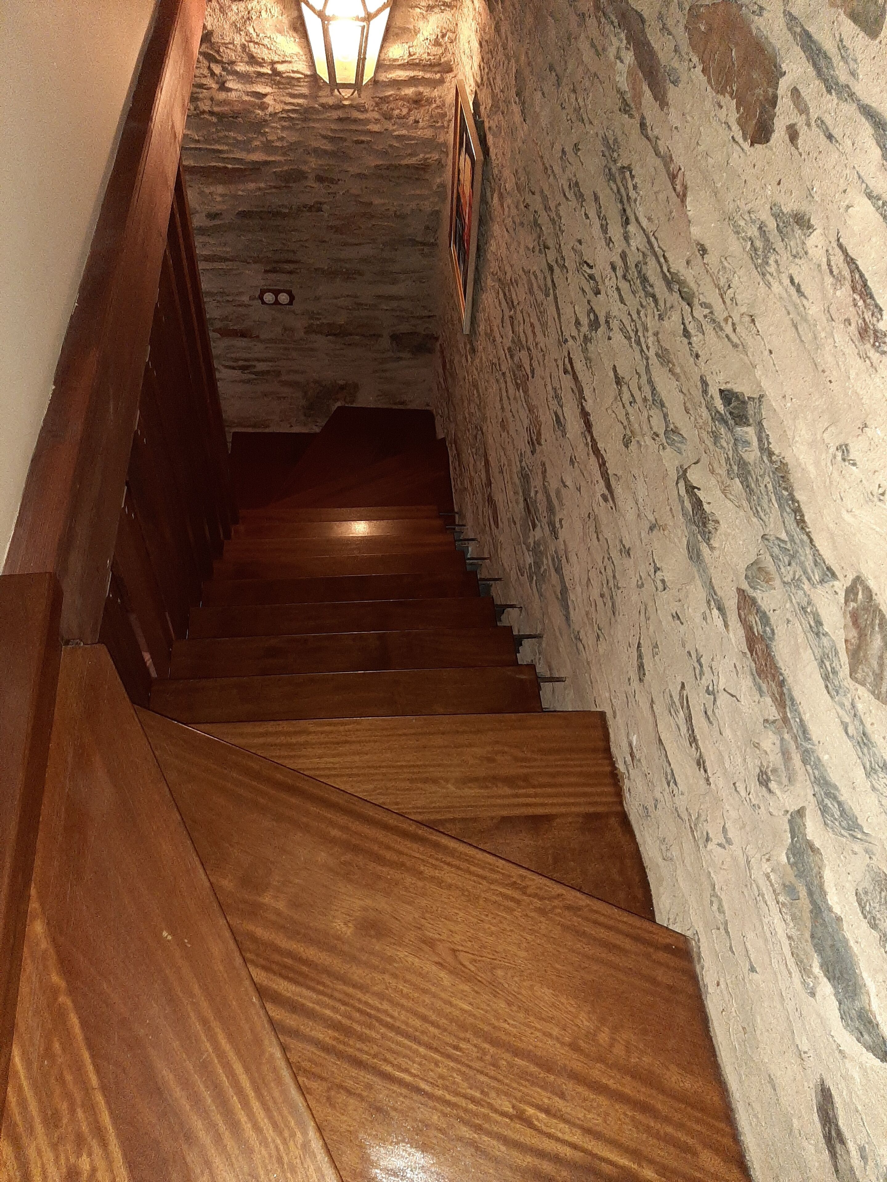A wooden staircase with stone walls and a light fixture at the top.