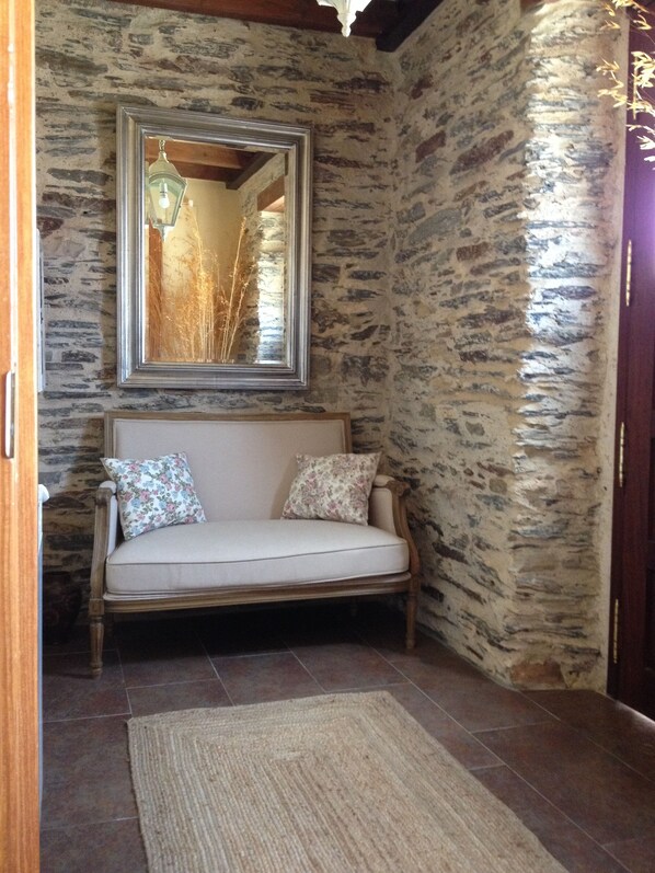 Una habitación con paredes de piedra, un sofá de madera y un espejo encima.