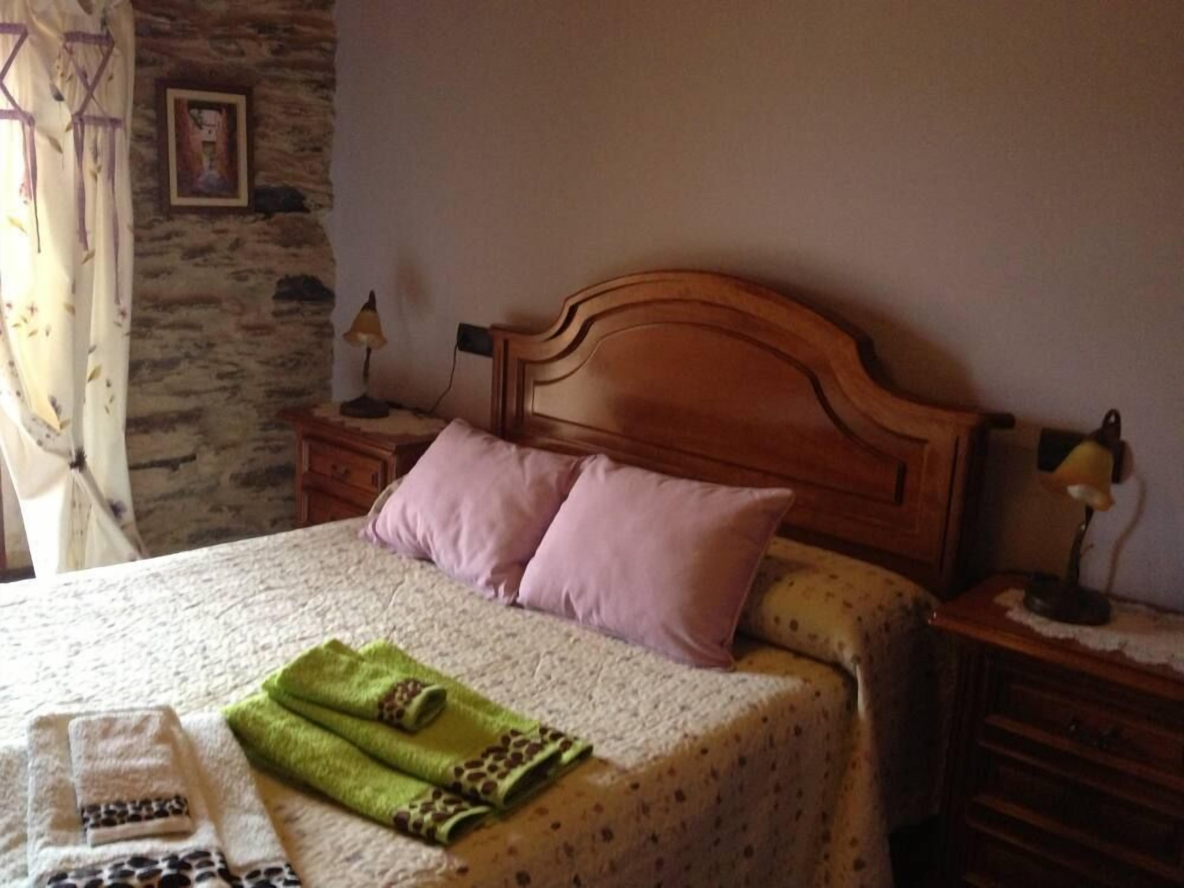 Une chambre à coucher avec une tête de lit en bois, deux lampes de chevet, un lit recouvert d’une couvre-lit à motifs et une serviette verte à imprimés d’animaux.