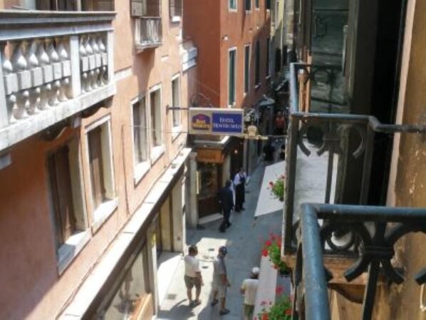 A narrow street with buildings on either side, a sign for a hotel, and a few pedestrians.