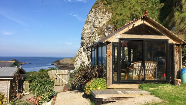 Una cabaña de madera frente al mar con puerta de cristal, una silla en el interior y vistas al océano.