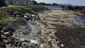 Escena costera con un edificio blanco, costa rocosa y mar tranquilo.