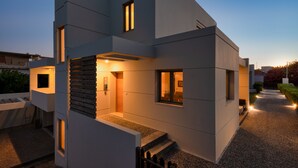 Een modern huis met twee verdiepingen, een schuin dak, een trap naar de bovenverdieping en een klein buitenplaatsje met een bankje.