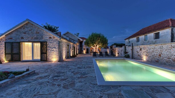 Un patio de piedra con piscina, edificios de piedra y mobiliario de exterior.