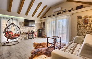 A cozy living room with a stone wall, a hanging chair, a wooden table, and a sofa. - Holiday House Oliva - with a private pool and 10 min to the beach by MyWaycation (Podlug)