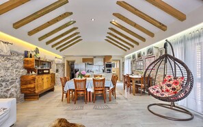 A spacious dining area with wooden beams, a stone wall, and a hanging chair. - Holiday House Oliva - with a private pool and 10 min to the beach by MyWaycation (Podlug)
