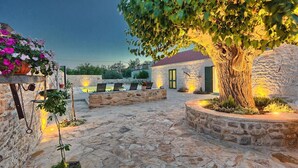 Un patio de piedra con un árbol, mobiliario exterior y un edificio con techo de tejas rojas.