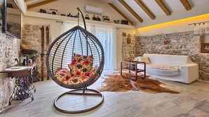 Un salón acogedor con una silla colgante, un sofá blanco, una pared de piedra y un techo de madera.