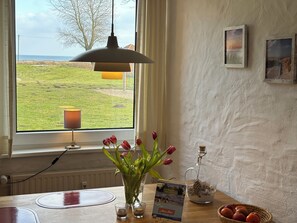 Ett rum med ett stort fönster, ett bord med en vas med tulpaner, ett ljus, en glasburk med snäckskal och en korg med apelsiner.