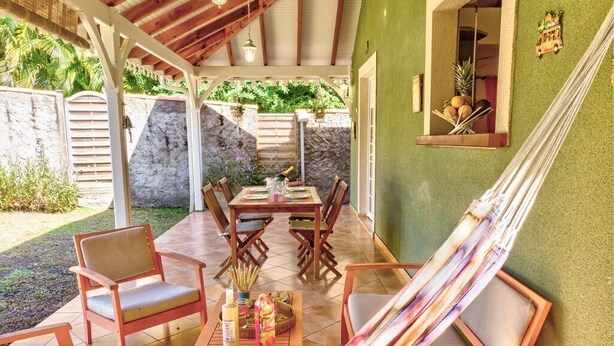 Une terrasse extérieure avec des meubles en bois, un hamac et une table où sont disposées des boissons et des collations.