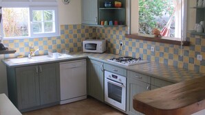 Une cuisine compacte équipée d’un four à micro-ondes, d’une cuisinière et d’un évier. Une fenêtre offre une vue sur la verdure environnante.