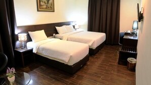 A hotel room with two beds, a desk, a chair, a lamp, a picture on the wall, and a trash bin. - Continent Centrepoint Hotel Makassar (Makassar)