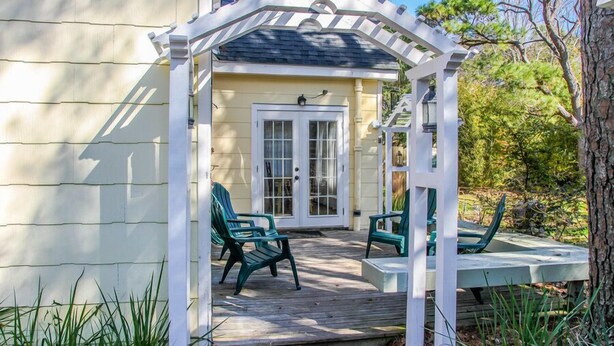 Un portico coperto con due poltrone Adirondack verdi e una struttura a pergola bianca.