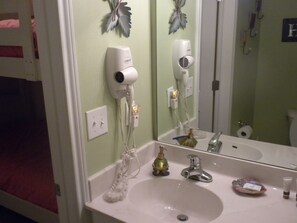 A bathroom with a white sink, a mirror, a hairdryer, and a bottle of shampoo.