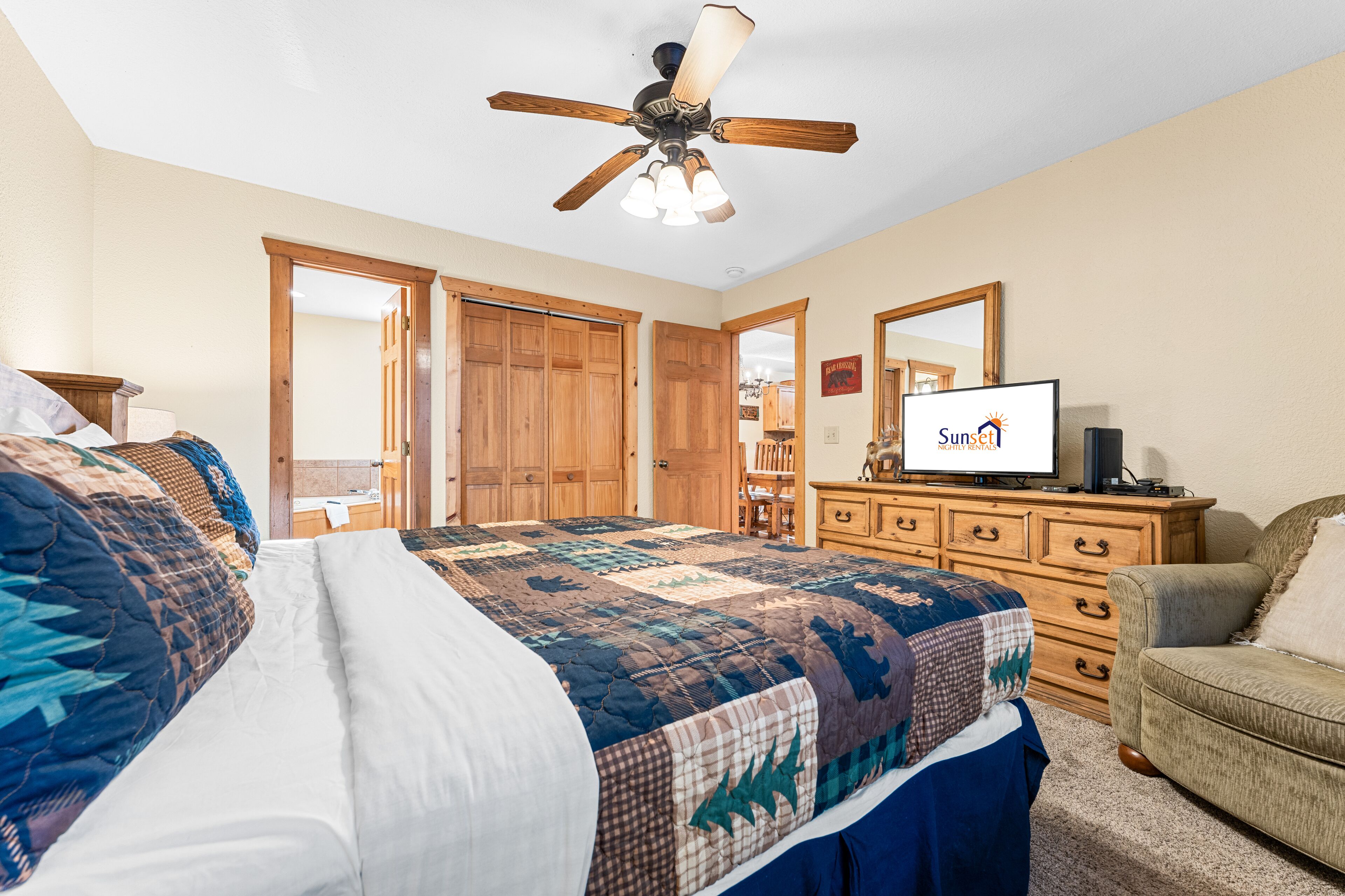 A bedroom with a large bed, a ceiling fan, wooden doors, a dresser, and a television.