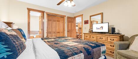 A bedroom with a large bed, a ceiling fan, wooden doors, a dresser, and a television.