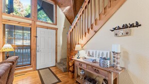 Una escalera de madera con un letrero de 'Welcome' y adornos de pájaros, un banco de madera, un perro sosteniendo un letrero de 'Welcome', y una consola con una lámpara y una cesta de bayas.