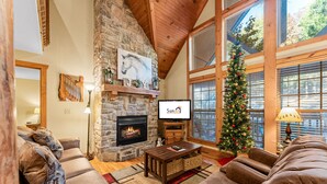 Una sala de estar acogedora con chimenea de piedra, sofás de cuero, un árbol de Navidad y un televisor.