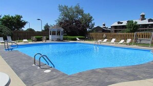 Ein rechteckiger Pool mit einer gefliesten Liegefläche, umgeben von Liegestühlen und einem Pavillon.