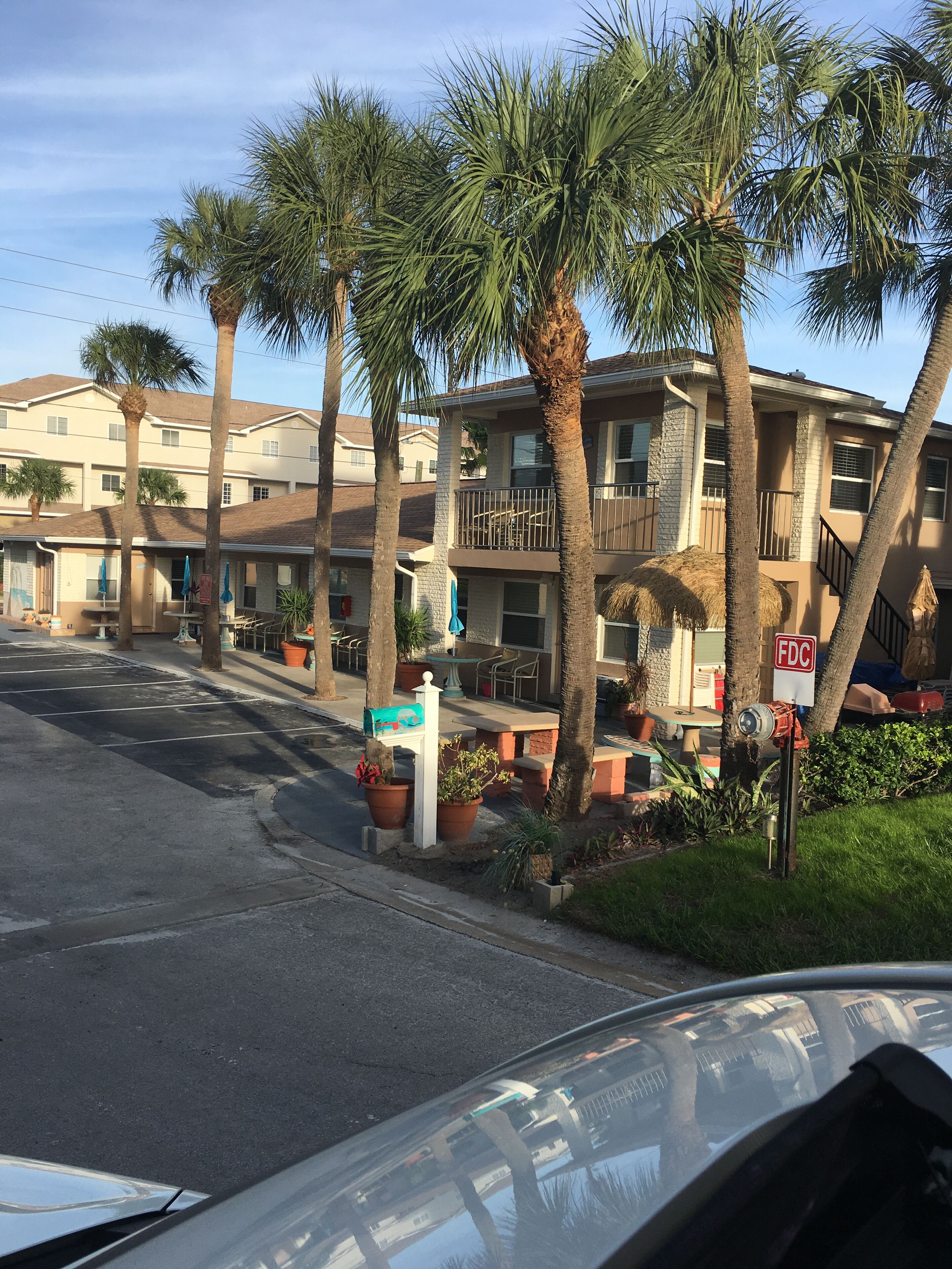 A residential area with a multi-story building, palm trees, and a street with parked cars.