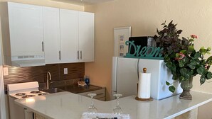 Una cocina con armarios blancos, una isla blanca con taburetes de bar, un refrigerador y una planta en maceta.