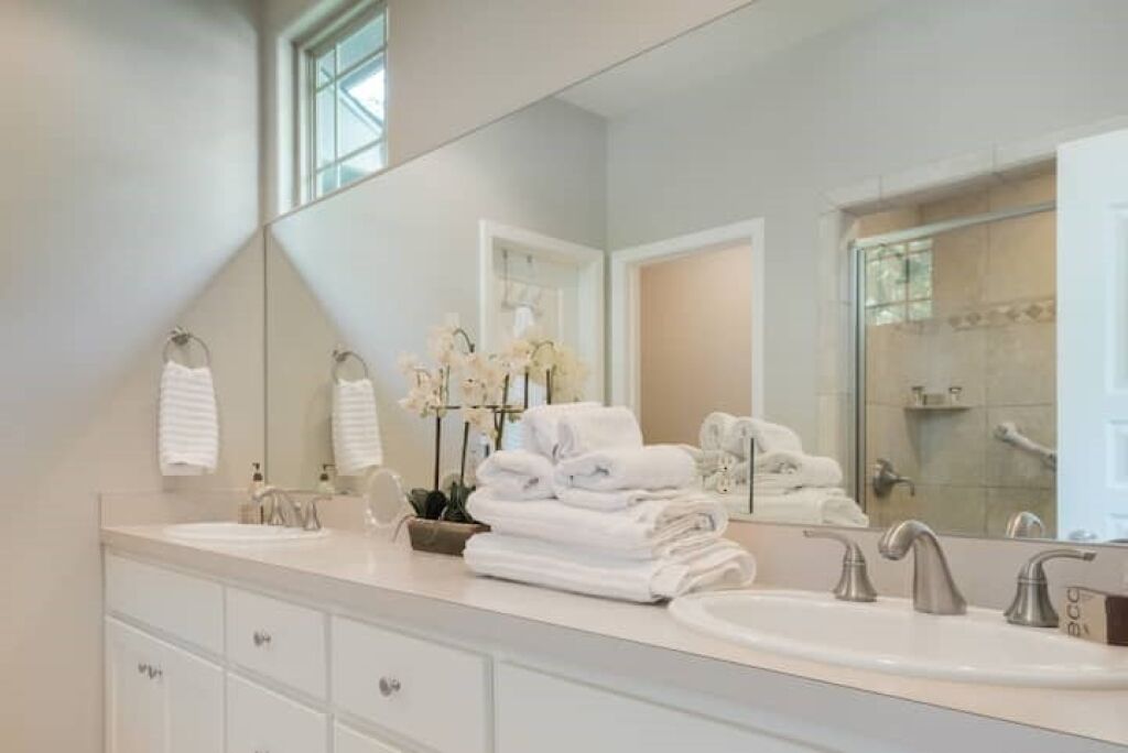 Une salle de bain moderne avec un grand miroir, deux lavabos et une pile de serviettes.